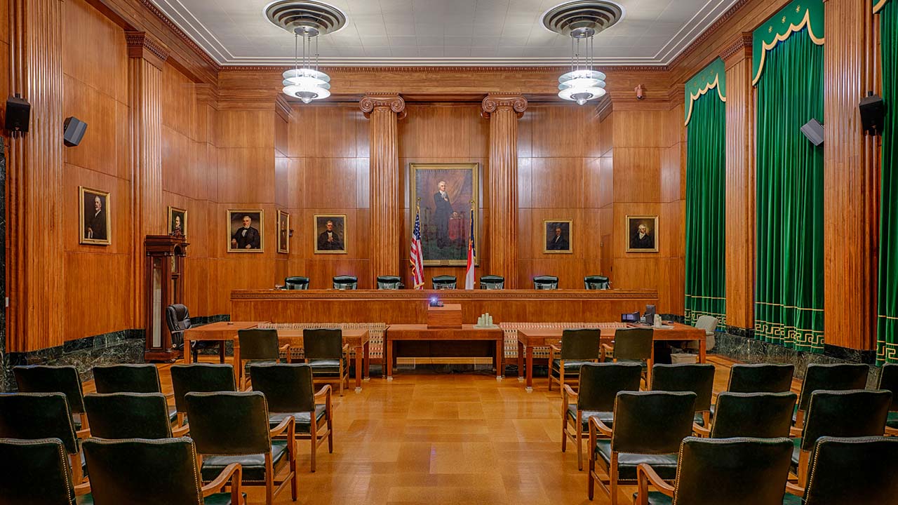 Interior photo of an empty court room with wood paneling walls, wood floor and paintings on walls.